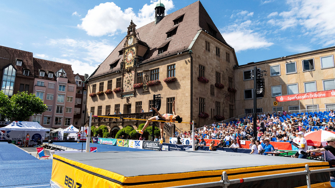 Das Bild zeigt eine Hochspringerin, wie sie in der Arena auf dem Marktplatz vor den Zuschauertribünen die Latte überquert. 