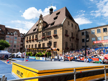 Das Bild zeigt eine Hochspringerin, wie sie in der Arena auf dem Marktplatz vor den Zuschauertribünen die Latte überquert. 