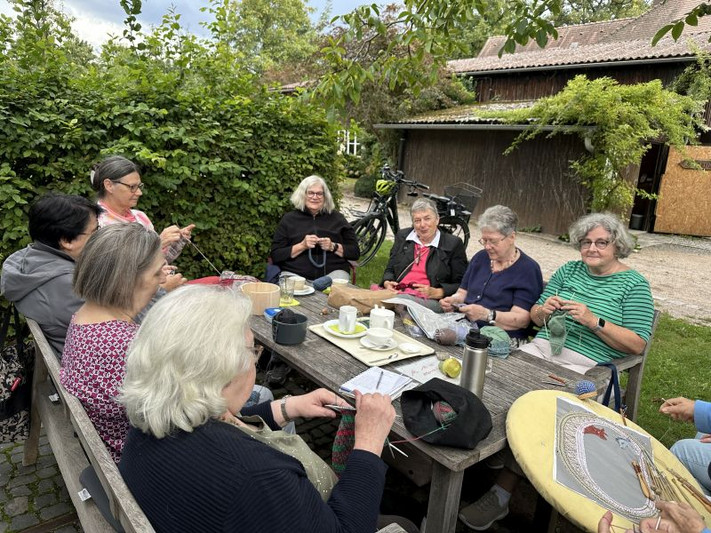 Das Bild zeigt eine Gruppe Frauen mit Stricknadeln an einem Holztisch im Botanischen Obstgarten.