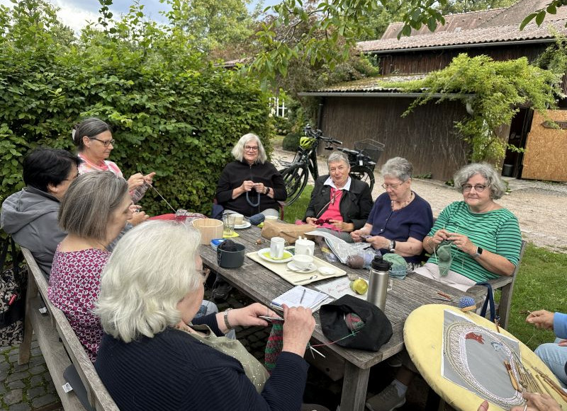 Das Bild zeigt eine Gruppe Frauen mit Stricknadeln an einem Holztisch im Botanischen Obstgarten. 