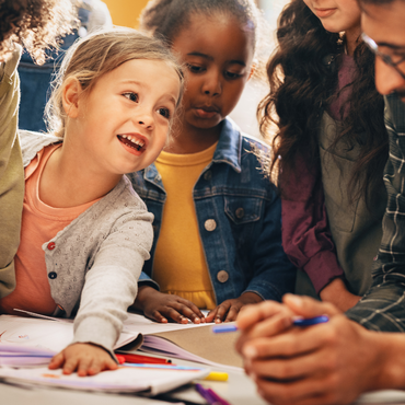 Mehrere Kinder sitzen gemeinsam an einem Tisch und schauen in ein Buch während sie lernen