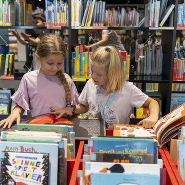 Man sieht zwei Kinder, die Bücher in der Stadtbibliothek aussuchen