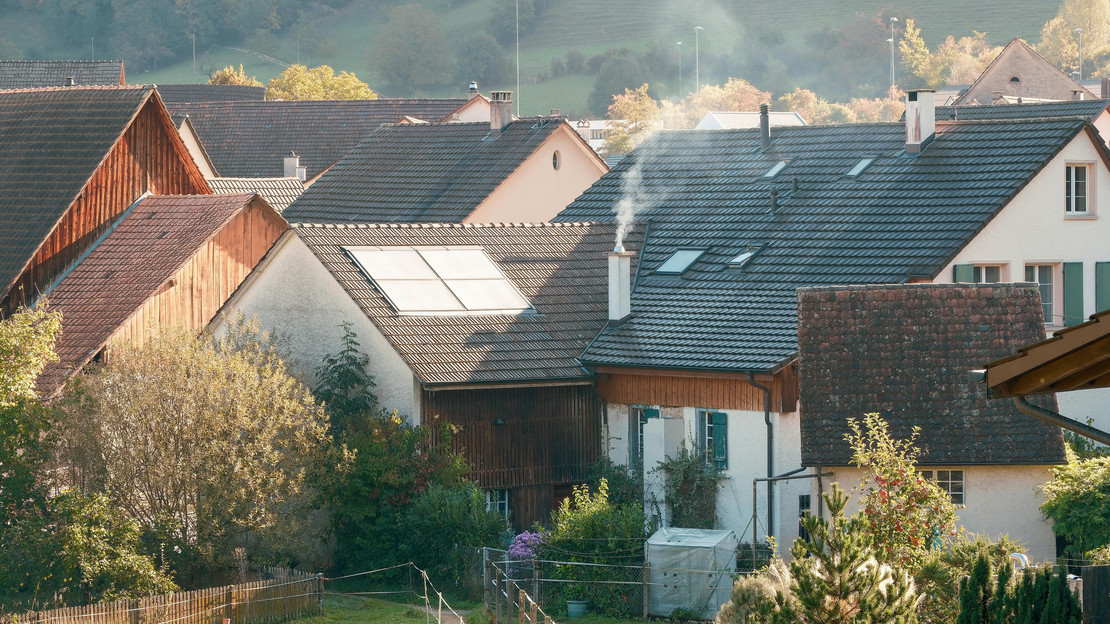 Auf dem Foto sind mehrere Einfamilienhäuser im Frühjahr zu sehen. Der Schornstein eines Hauses raucht.