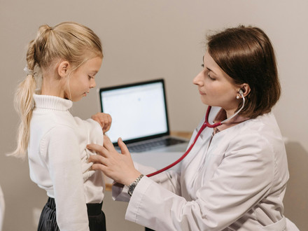 Das Bild zeigt eine Kinderärztin in weißer Arbeitskleidung, die ein junges Mädchen abhört.