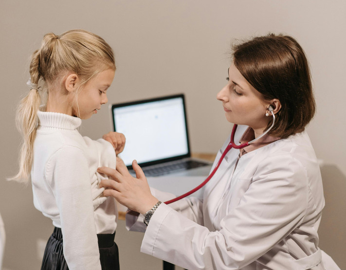 Das Bild zeigt eine Kinderärztin in weißer Arbeitskleidung, die ein junges Mädchen abhört.