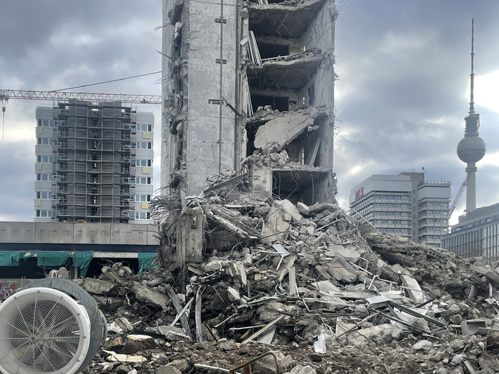 Das Bild zeigt ein Abrisshaus mit viel Trümmerschutt inmitten einer Großstadt neben moderneren Hochhäusern.