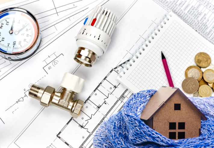 Man sieht einen symbolischen Plan, Heizungsteile und ein Haus mit Schal