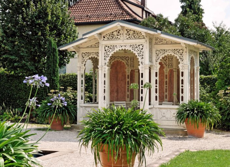 Das Bild zeigt eine kunstvoll verzierte Gartenlaube, die auf dem Gelände steht. 