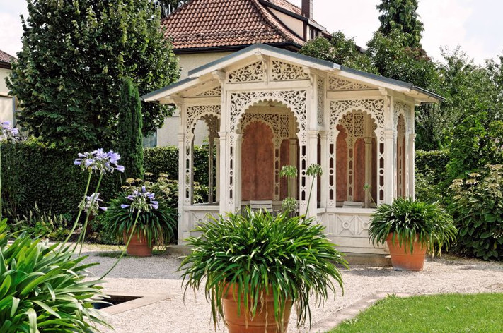 Das Bild zeigt eine kunstvoll verzierte Gartenlaube, die auf dem Gelände steht.