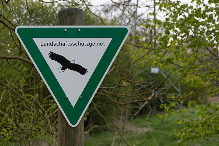 Das Bild zeigt ein grün-weißes Schild in Dreiecksform, das vor Ort auf ein Landschaftsschutzgebiet hinweist.