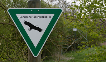 Das Bild zeigt ein grün-weißes Schild in Dreiecksform, das vor Ort auf ein Landschaftsschutzgebiet hinweist.