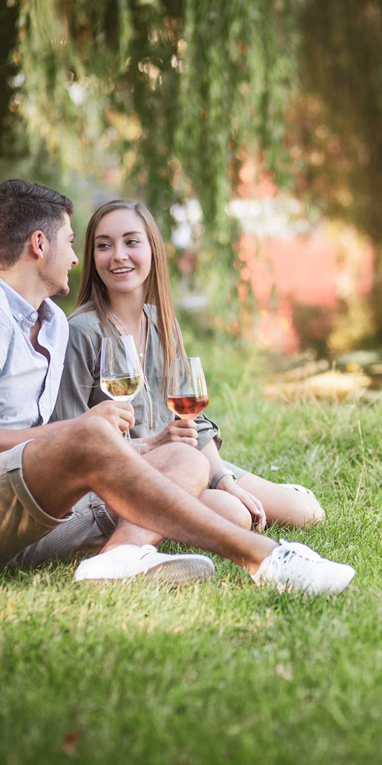 Ein Pärchen sitzt am Neckar und trinkt ein Glas Wein