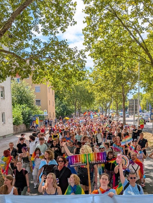 Teilnehmende beim Christopher Street Day ziehen mit Regenbogenflaggen und Bannern durch eine Straße in Heilbronn begleitet von vielen Menschen entlang der Route.