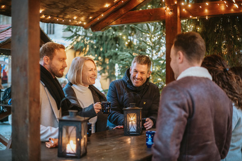 Zwei Frauen und drei Männer trinken Glühwein auf dem Weihnachtsmarkt. 