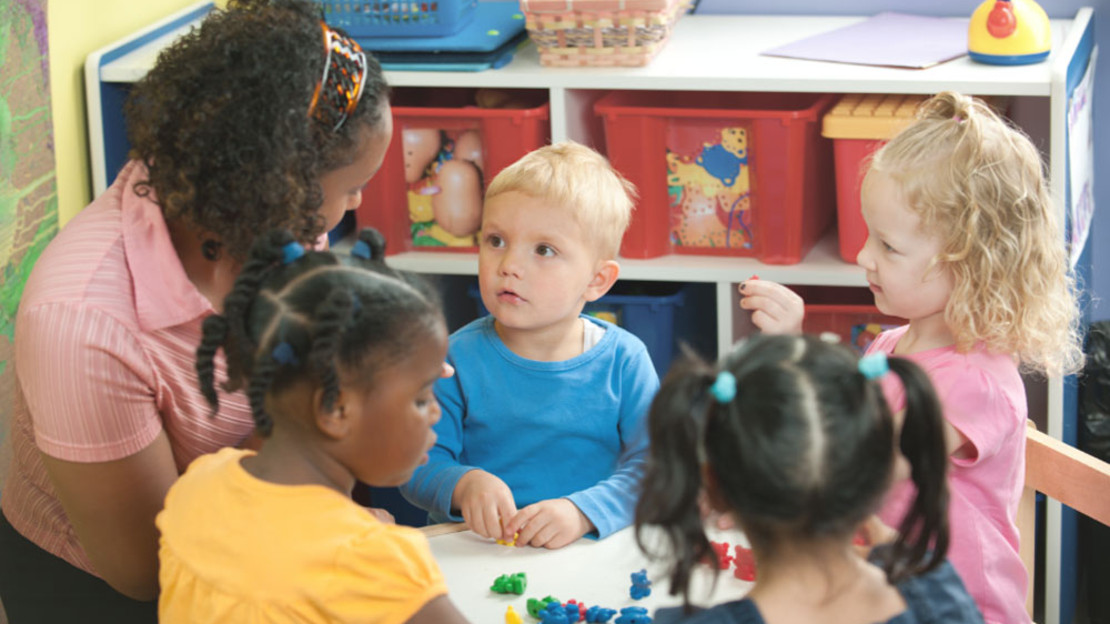Vier Kindergartenkinder mit einer Erzieherin im Kindergarten