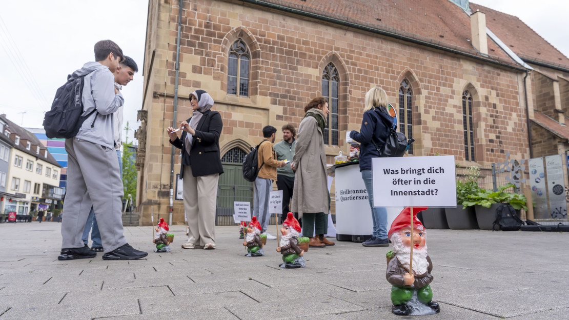 Das Bild zeigt den Infostand der Bürgerbeteilgung in der Sülmerstraße. Dort kommen Mitarbeitende der Stadt mit Bürgerinnen und Bürgern zur Entwicklung der Innenstadt und des neuen Quartiersbüros ins Gespräch. Zwergfiguren mit Fragen zur Innenstadt machen auf den Stand aufmerksam. 