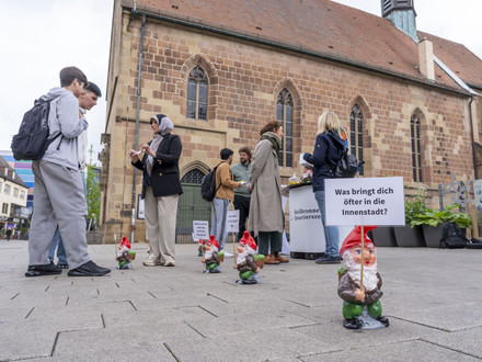 Das Bild zeigt den Infostand der Bürgerbeteilgung in der Sülmerstraße. Dort kommen Mitarbeitende der Stadt mit Bürgerinnen und Bürgern zur Entwicklung der Innenstadt und des neuen Quartiersbüros ins Gespräch. Zwergfiguren mit Fragen zur Innenstadt machen auf den Stand aufmerksam.