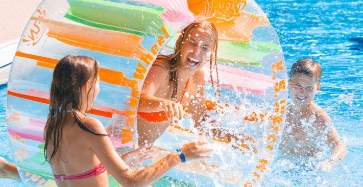 Das Bild zeigt Kinder und Jugendliche in einem Freibad-Becken, wie sie mit viel Spaß im Wasser herumtollen.
