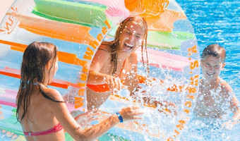 Das Bild zeigt Kinder und Jugendliche in einem Freibad-Becken, wie sie mit viel Spaß im Wasser herumtollen. 