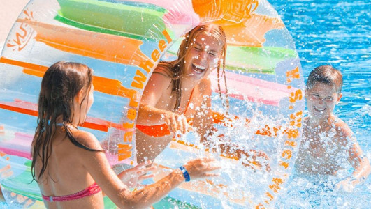Das Bild zeigt Kinder und Jugendliche in einem Freibad-Becken, wie sie mit viel Spaß im Wasser herumtollen. 