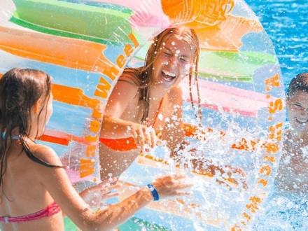 Das Bild zeigt Kinder und Jugendliche in einem Freibad-Becken, wie sie mit viel Spaß im Wasser herumtollen. 