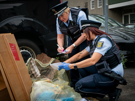 Das Bild zeigt eine Streife der Waste Watcher mt zwei Frauen, die illegal abgelegten Müll nach Hinweisen auf den Verursacher durchsuchen. 
