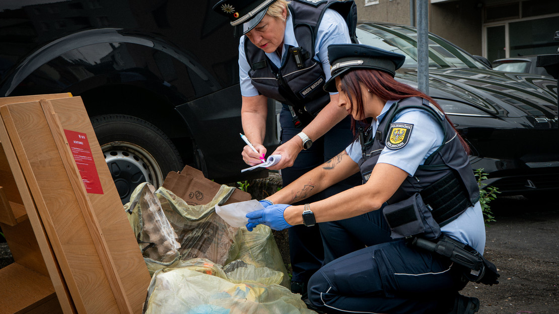 Das Bild zeigt eine Streife der Waste Watcher mt zwei Frauen, die illegal abgelegten Müll nach Hinweisen auf den Verursacher durchsuchen. 