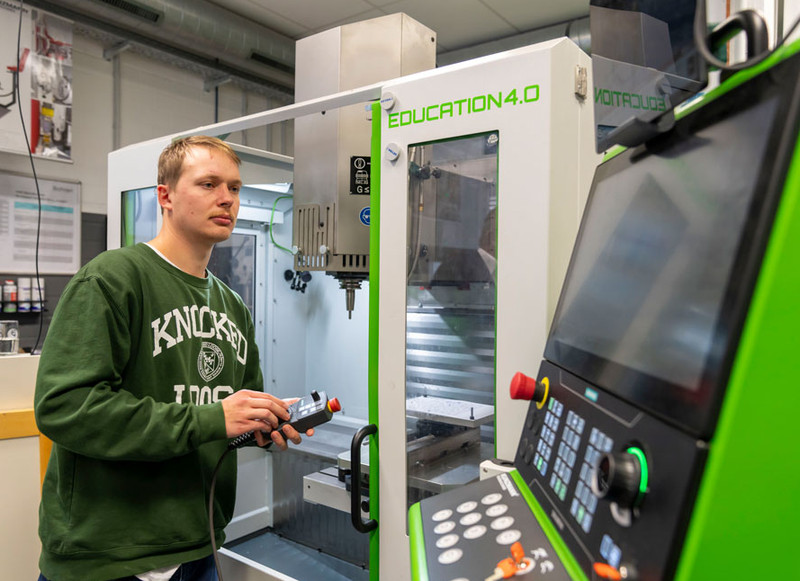 Über Bedienelement und Bildschirm steuert ein Fachschüler eine Fräsmaschine.