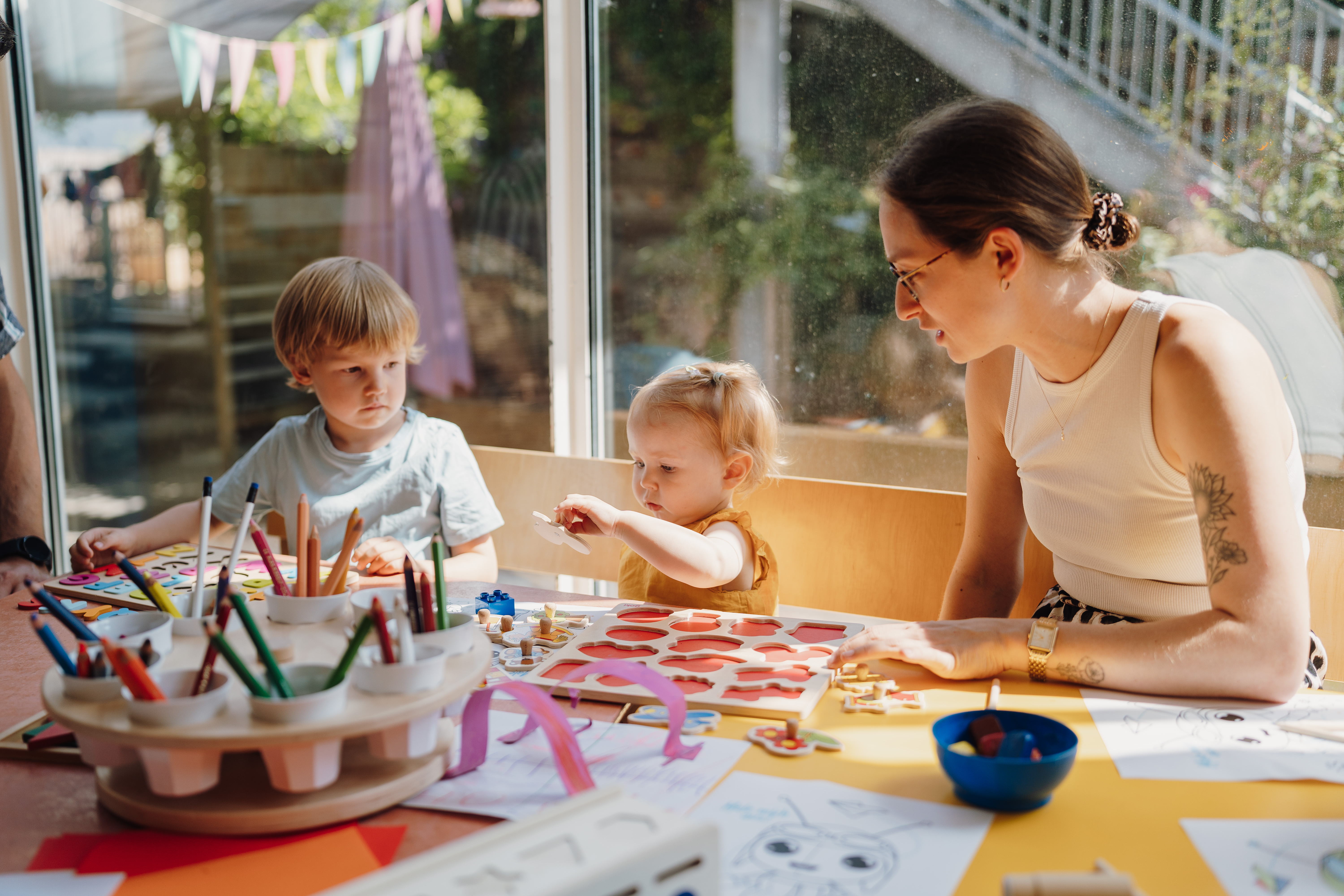 Man sieht eine Erzieherin des Kinderhauses Villa Rosa, die mit zwei Kindern malt. Foto: Akademie für Innovative Bildung und Management
