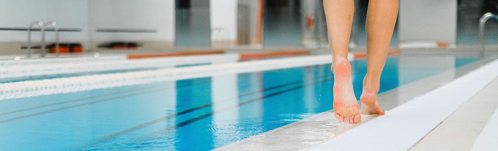 erson am Beckenrand eines Schwimmbads, die mit den Füßen ins Wasser steigt.