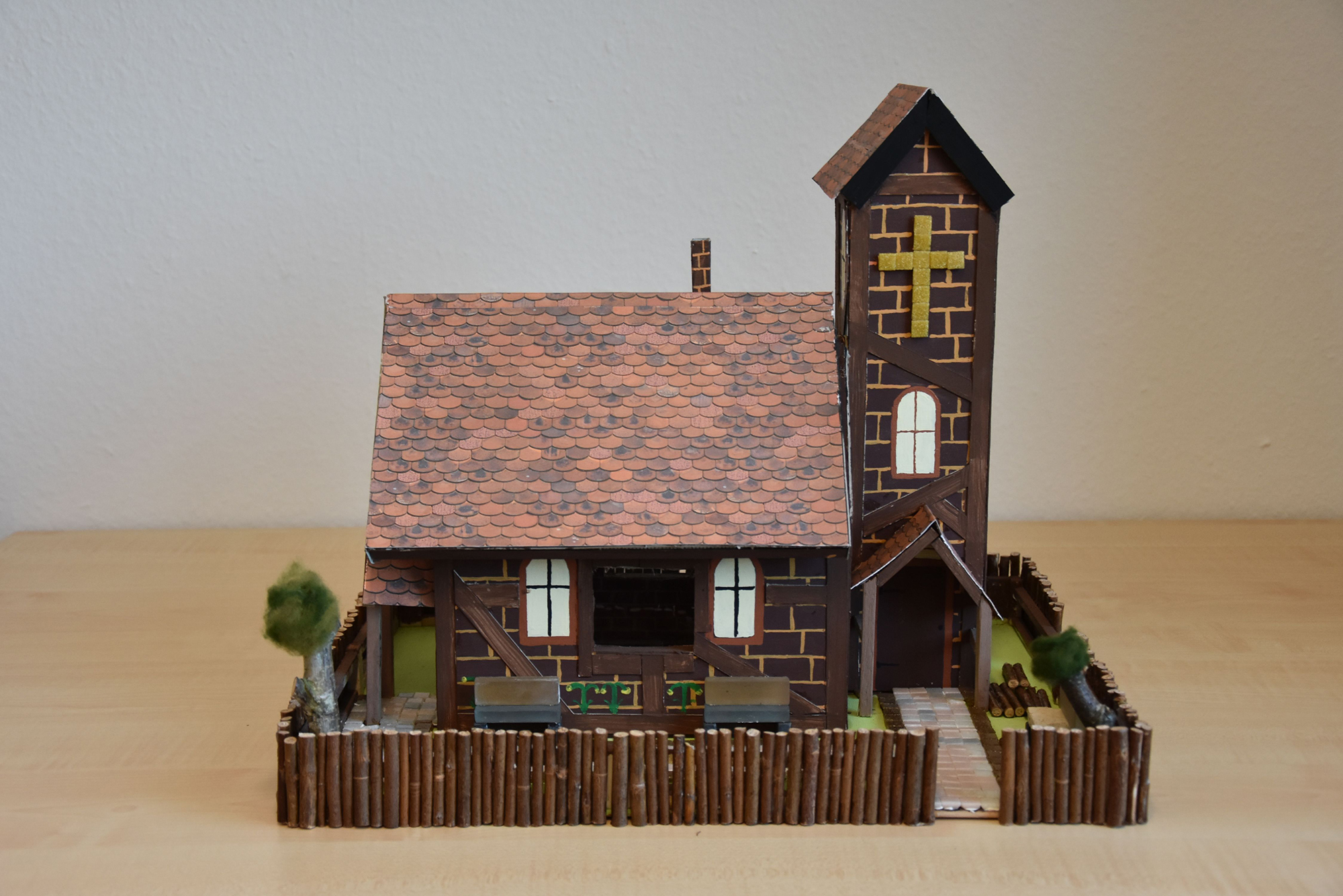 Die Miniatur eines braunen Kirchengebäudes aus verschiedenen Materialien mit Kirchturm und Satteldach umgeben von einem Zaun