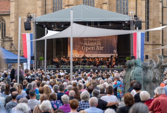 Menschen stehen vor einer Bühne auf dem Kiliansplatz. Dort spielt ein Orchester