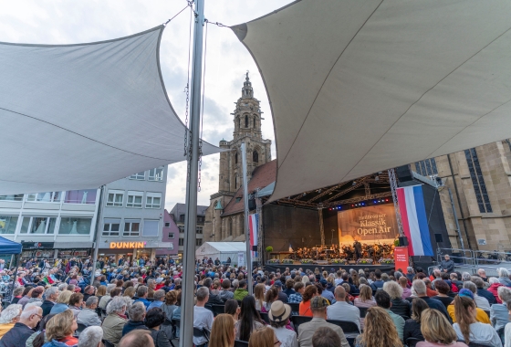 Menschen stehen vor einer Bühne auf dem Kiliansplatz. Dort spielt ein Orchester