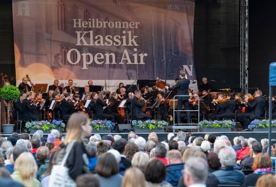 Menschen stehen vor einer Bühne auf dem Kiliansplatz. Dort spielt ein Orchester