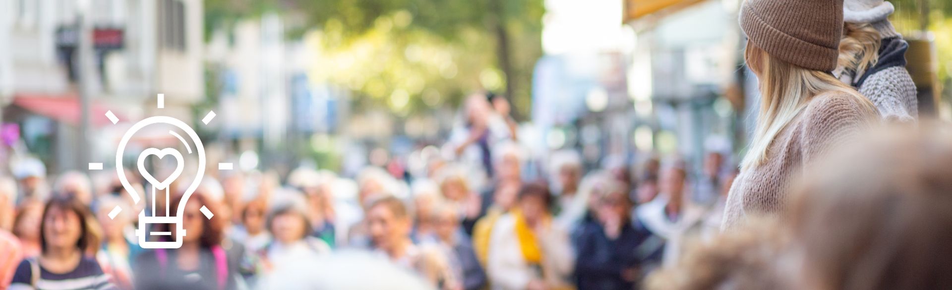 Man sieht viele Menschen sowie ein Glühbirnen-Icon mit Herz in der Mitte