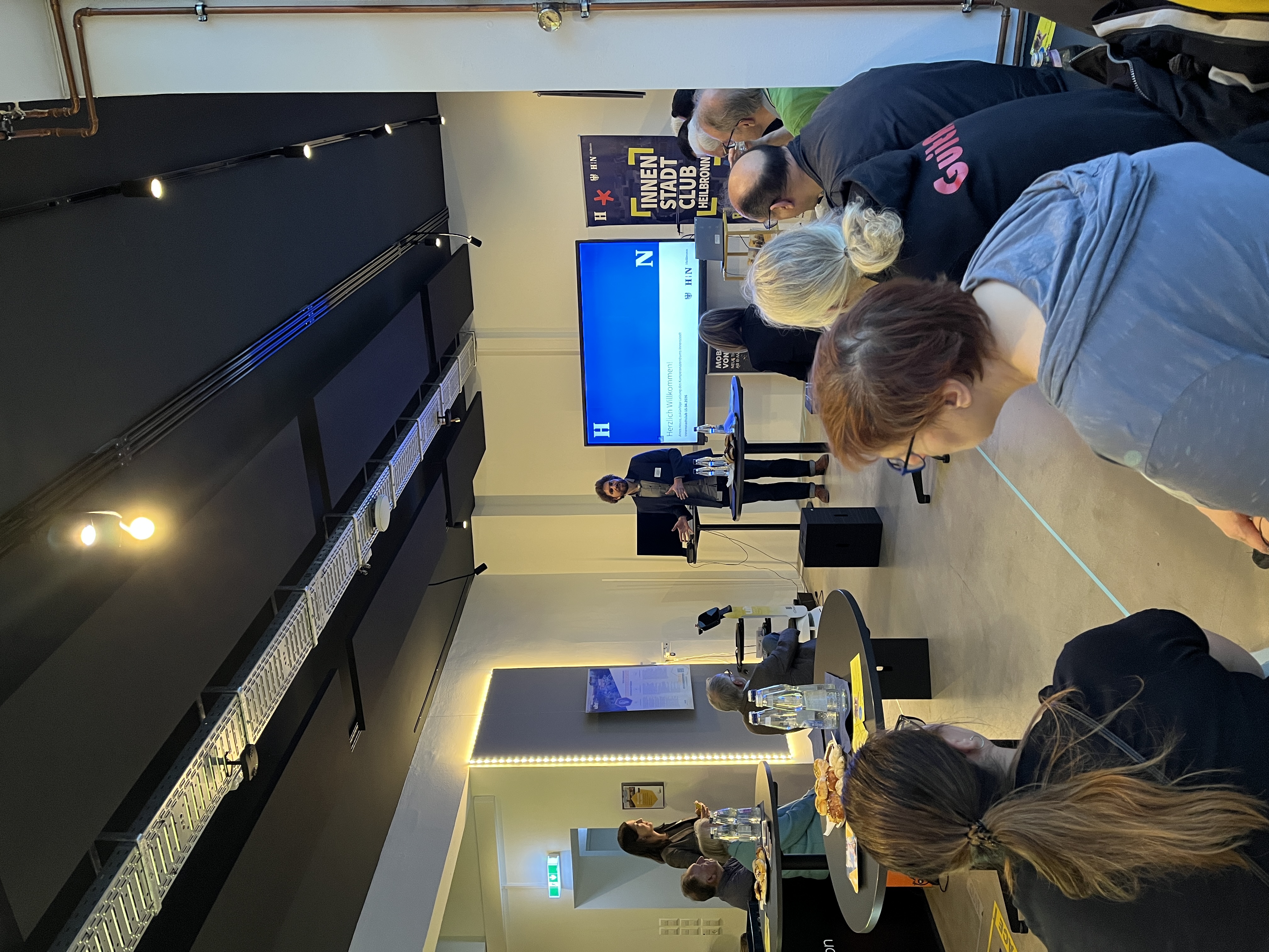 Vorstellung in einem Veranstaltungsraum: Amos Heuss präsentiert sich als neuer Leiter des Kompetenzzentrums Innenstadt vor Publikum. Die Teilnehmenden verfolgen den Vortrag, im Hintergrund sind Präsentationsbildschirm und ein Banner zum Innenstadt Club Heilbronn zu sehen.