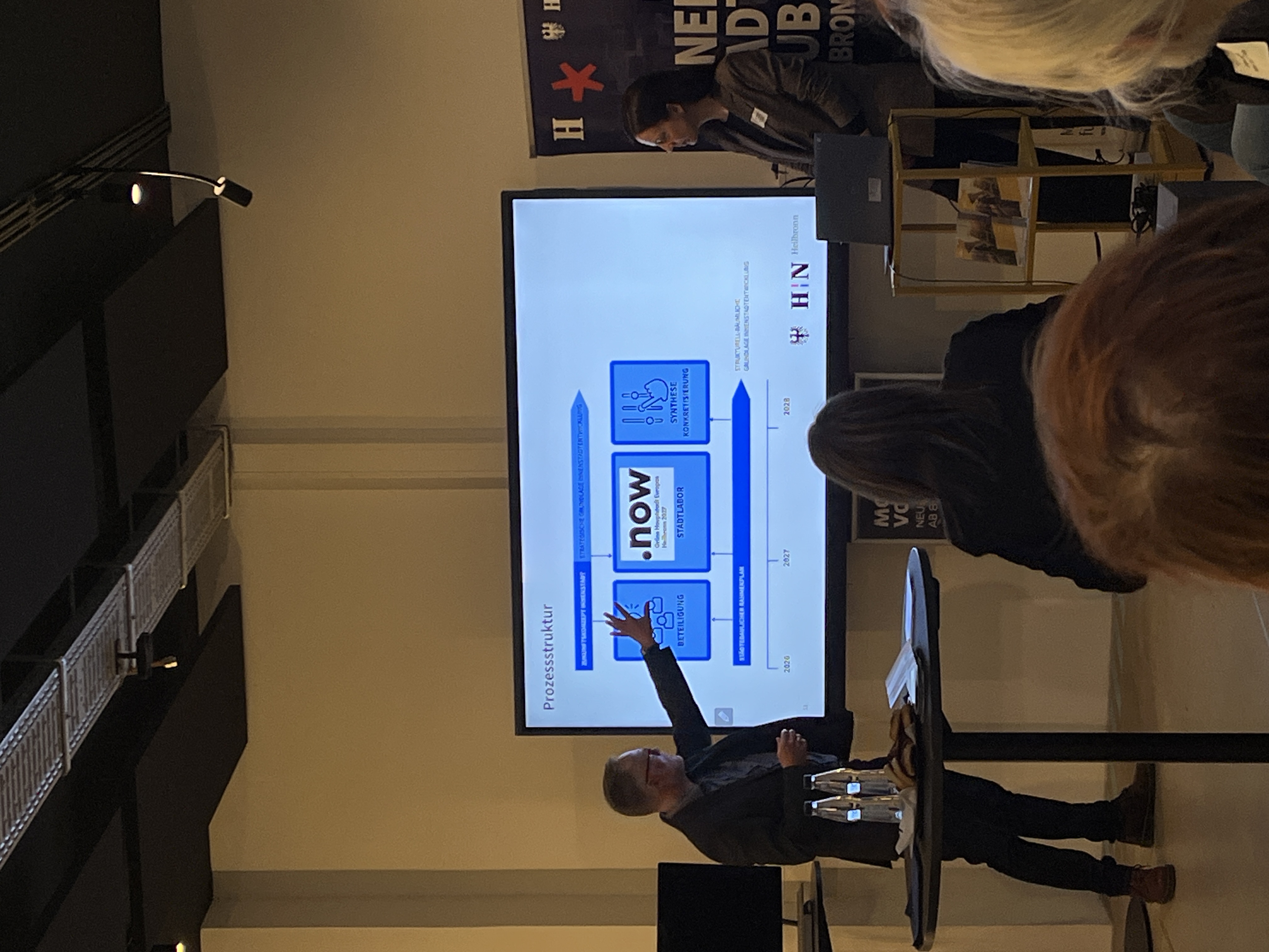 Präsentation in einem Veranstaltungsraum: Patrik Henschel vom Planungs und Baurechtsamt erläutert anhand einer Folie den Beteiligungsprozess für das Zukunftskonzept Innenstadt und den städtebaulichen Rahmenplan, während Teilnehmende zuhören.